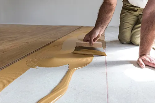 Installer spreading flooring adhesive with a notched trowel to glue down wood planks during a professional installation in Florida